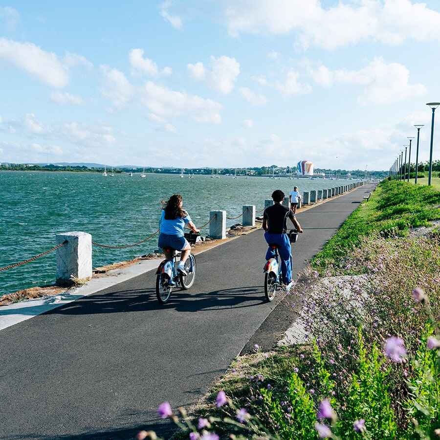 Two students riding bikes on the bike path next to the water.