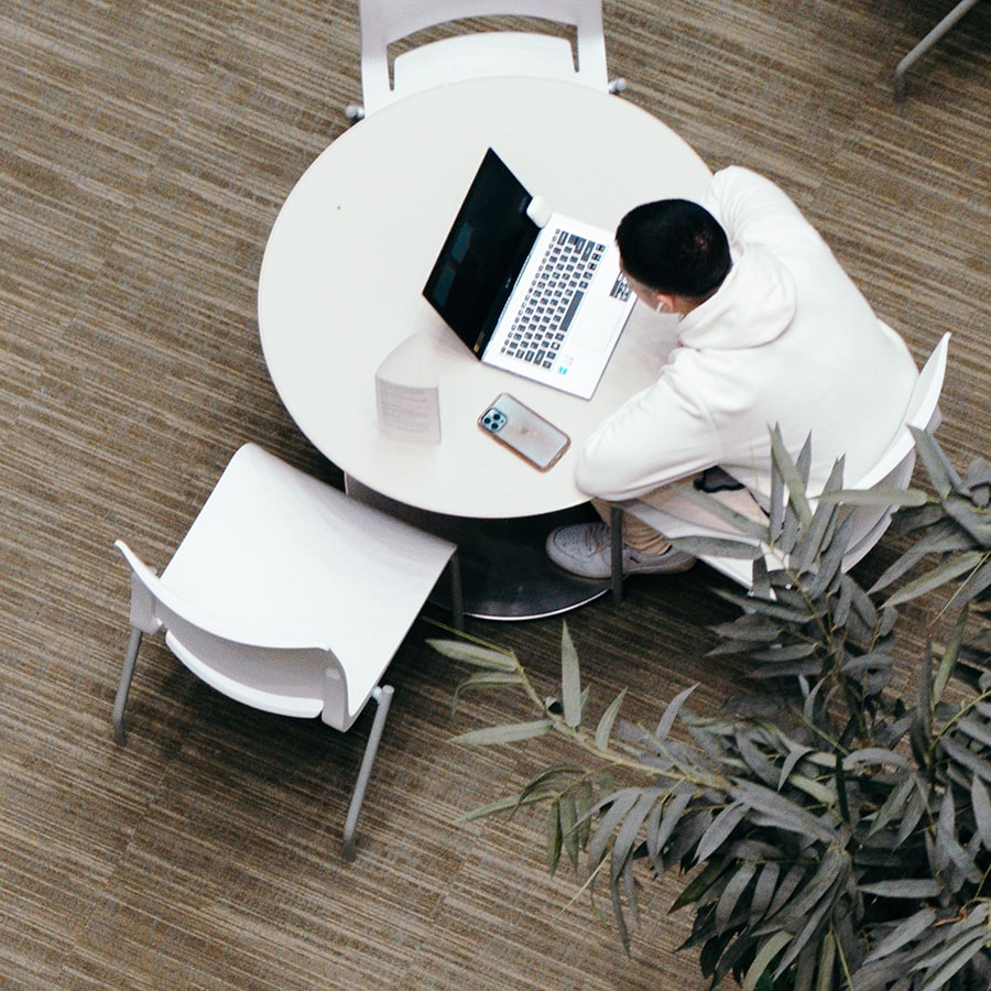 balcony view in Campus Center of student seated below at table using laptop