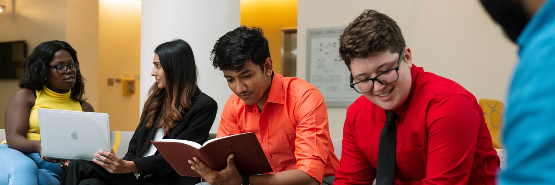 College of Management students informally sitting on couch reading a book, reviewing laptop and conferring