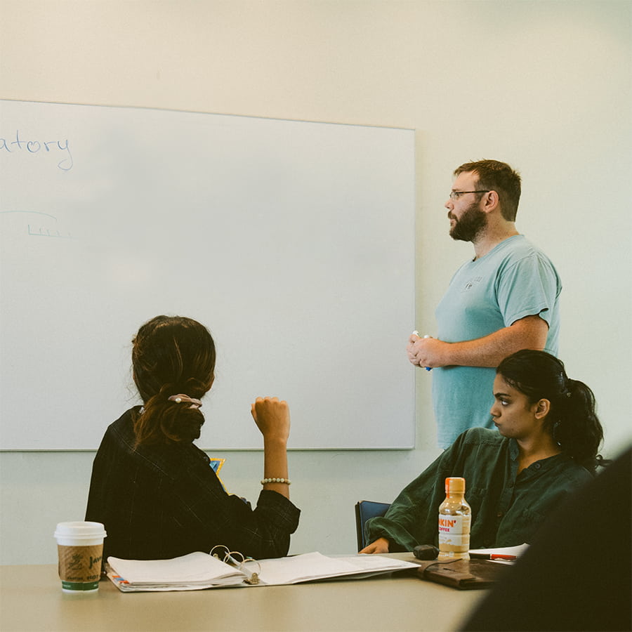 Student writing on the white board in front of other students.