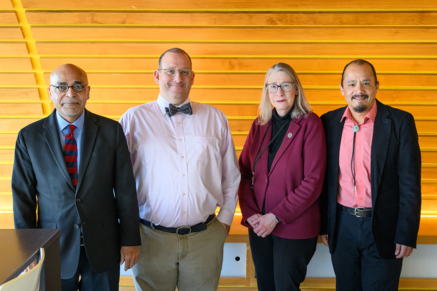 The PIs on the U54 grant that supports the cancer partnership stand in front of a wooden wall. From left to right, they are K. Viswanath, Gregory Abel, Jill Macoska, and Adán Colón-Carmona.
