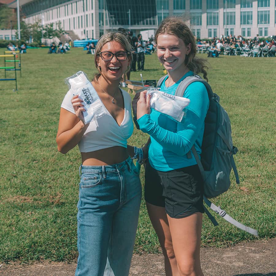 Two students hold recreation swag socks on campus center lawn.