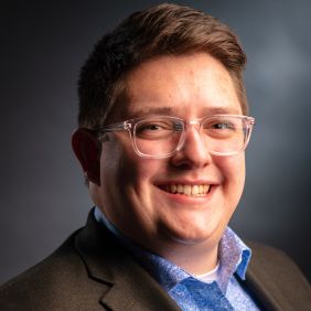 Man with short brown hair, glasses, blue shirt, brown blazer